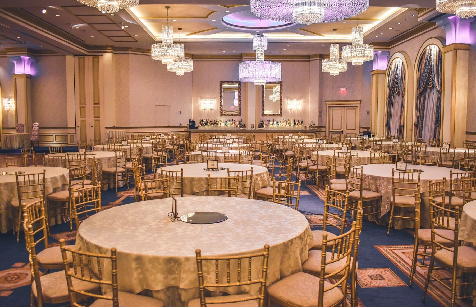 A banquet hall set with round tables and chandeliers